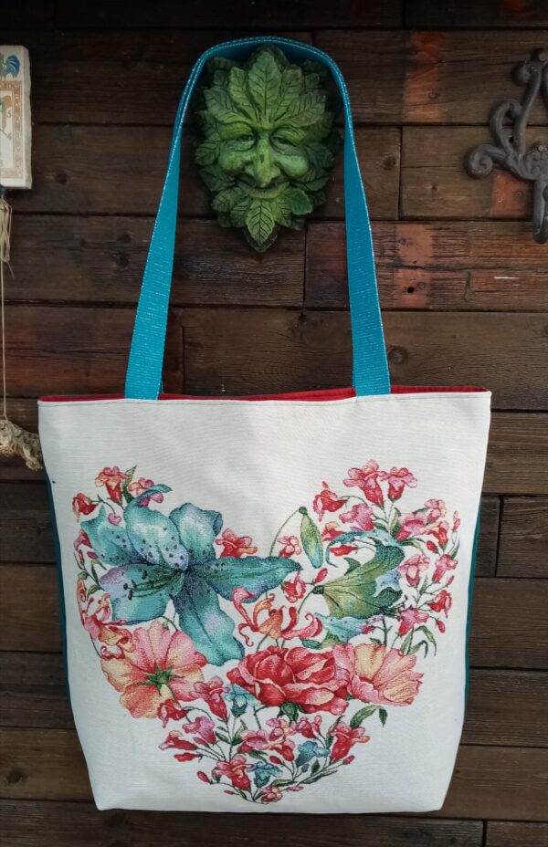 Le carré déco. Un sac grand format presque carré fait d'un coupon jacquard devant et de toile de coton à l'arrière du sac. Intérieur en coton style cretonne. Des anses en coton pailletée turquoise. Carré jacquard motif un gros coeur en fleur. Intérieur rouge. dos du sac turquoise. 2 poches intérieures. Cherchez le Chas