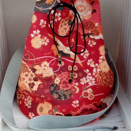 Sac sceau base ronde. Extérieur tissu renforcé en coton à motif japonais grues et fleurs sur fond rouge. Intérieur coton à petites fleurs. Sangle grise réglable. Une mini pochette assortie. Fermeture par un cordon noire passant par des œillets. Fond du sac renforcé semi rigide. Cherchez le Chas.