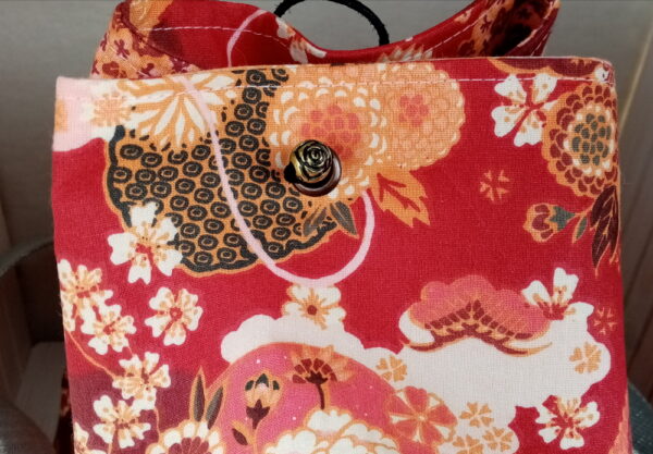 Sac sceau base ronde. Extérieur tissu renforcé en coton à motif japonais grues et fleurs sur fond rouge. Intérieur coton à petites fleurs. Sangle grise réglable. Une mini pochette assortie. Fermeture par un cordon noire passant par des œillets. Fond du sac renforcé semi rigide. Cherchez le Chas.